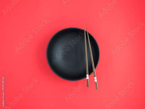 Black and shallow soup bowls, chopsticks, red background.