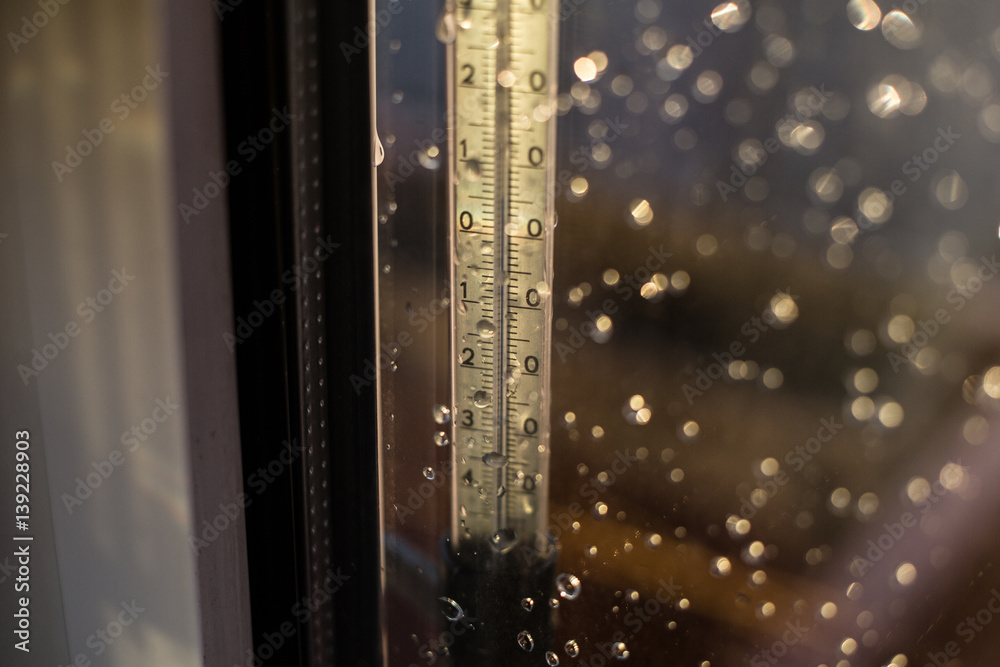 Fototapeta premium Fall in temperature on a thermometer scale. Drops of rain on window after a storm. Water drops on the glass after rain.