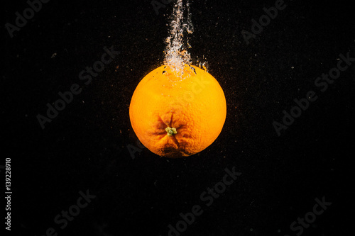 Juicy orange falls in water on black background