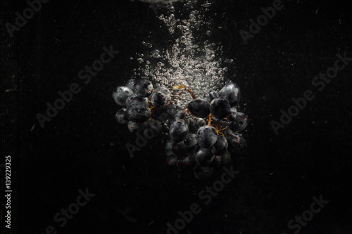 Heavy bunch of black grape falls in black aquarium
