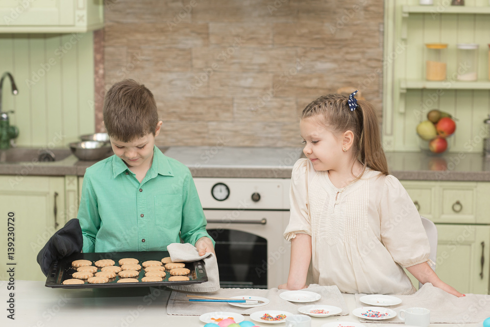 Fototapeta premium Cute kids baked cookies and tasting it at the table in the home kitchen