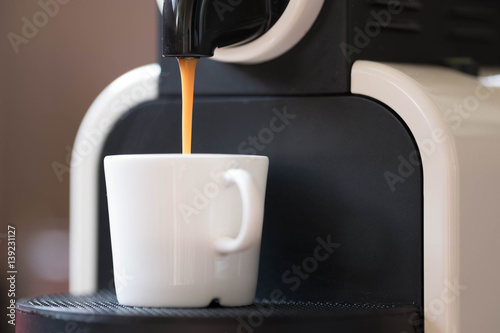 Espresso flow from coffee machine to white ceramic cup.