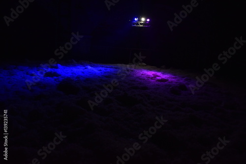 Floor covered by feathers after pillows war. Is is in a large dark room illuminated by three lights