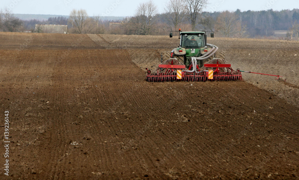 Fototapeta premium Tractor preparing land for sowing. Tractor with cultivator handles field before planting. Preparing land for sowing at spring, farmer in tractor.
