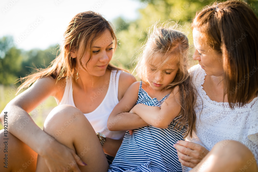 Mother and adult daughter comforting young girl child Mother and adult daughter comforting young girl child