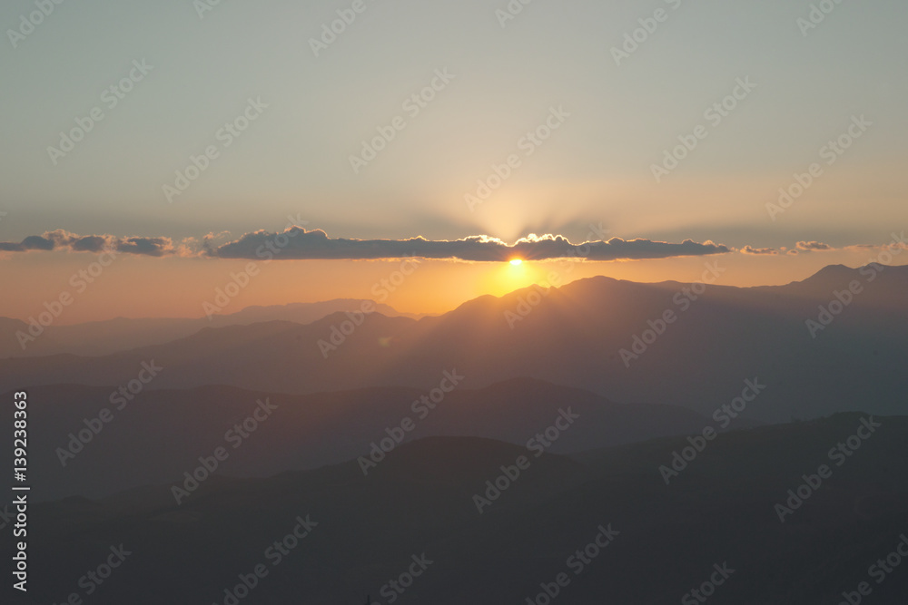 Sun setting behind the clouds and a silhouette of mountains at nightfall in China.