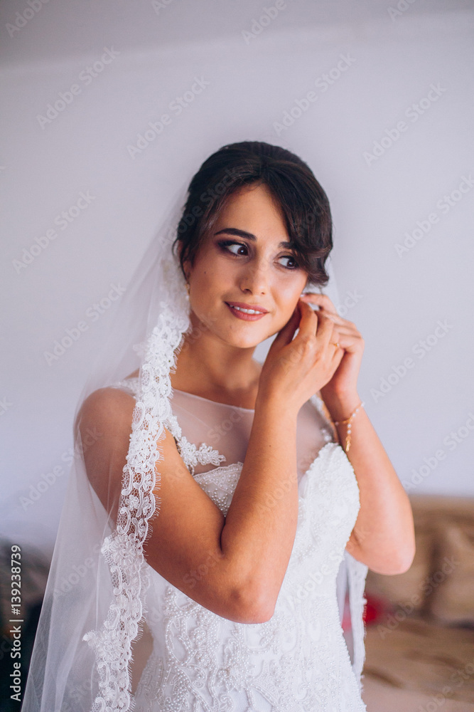 Wedding preparation. Beautiful, happy bride dresses earrings before wedding. Wedding accessories, jewelry. Closeup portrait of bride. Selective focus. Wedding preparation. Beautiful, happy bride dresses earrings before wedding. Wedding accessories, jewelry. Closeup portrait of bride. Selective focus.