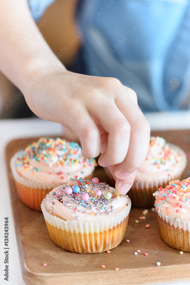 close up view of girl's hand decorating cupcakes with confetti
