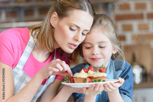 portrait of mother and daughter holding homemade cupcakes with strawberries