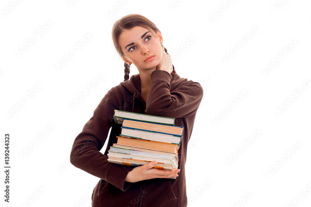 Teen girl with pigtails in the jacket looks up and holds a lot of books Teen girl with pigtails in the jacket looks up and holds a lot of books