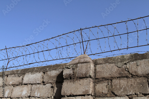 Barbed wire on top of the brick wall restricts the freedom of movement of people and protects the inviolability of private property.