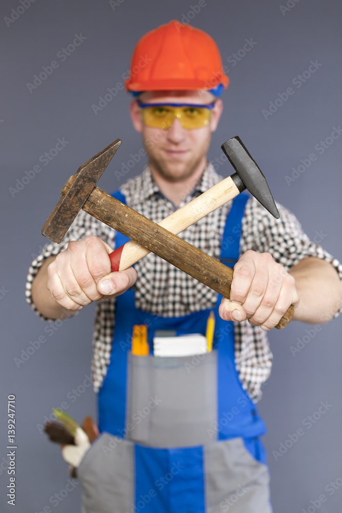 Vigorous young worker in uniform with two cross hammers in hands. Blurred figure Vigorous young worker in uniform with two cross hammers in hands. Blurred figure