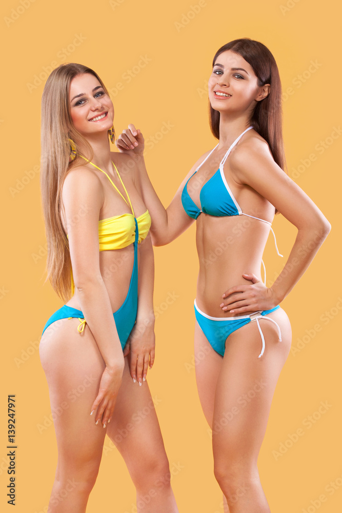Two sexy women in swimwear posing on orange background. Perfect body. Bikini  summer advertisement concept. Stock Photo | Adobe Stock