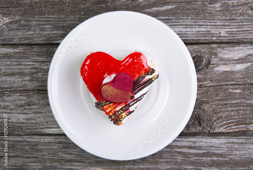 The dish is white with cake in shape of heart on wooden background