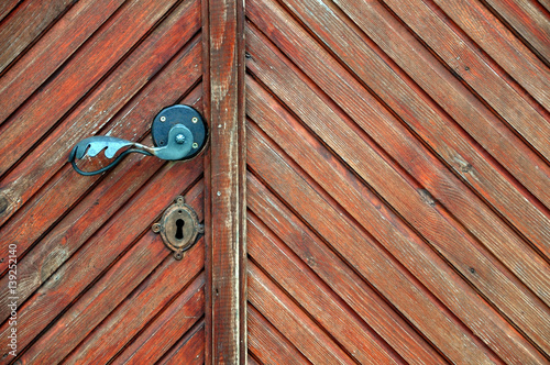 Diagonal texture of brown wooden door with old metal handle.