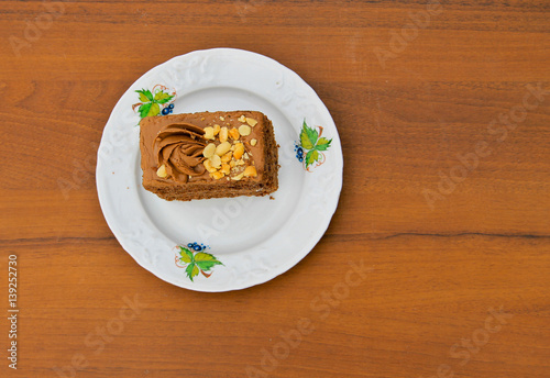 Piece of cake with nuts on plate on wooden table. Top view