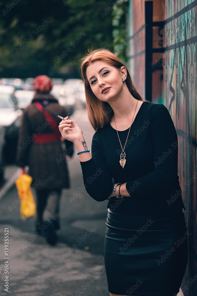 Happy woman smoking provocative on city street, leaning seductive next to  artsy wall. Wearing black leather skirt, long statement necklace, drawing  attention from the woman behind, to her. Stock Photo | Adobe