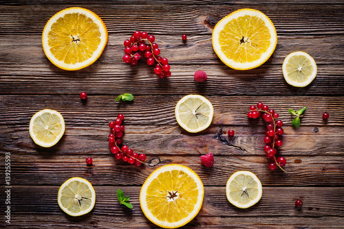 Lemon and orange rings  red currants  raspberries and mint leaves on wooden background. Table top view. Fresh fruit composition   layout.
