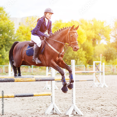 Young horseback sportswoman jumping over obstacles on show jumping competition