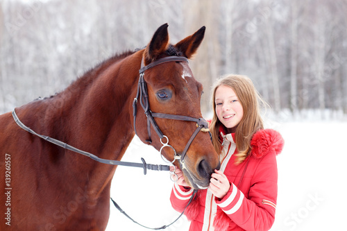 Young teenage girl spending time with her friend bay horse in winter park. Equestrian hobby background © skumer