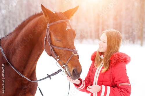 Teenage girl feeding bay horse on winter field. Friendship concept image