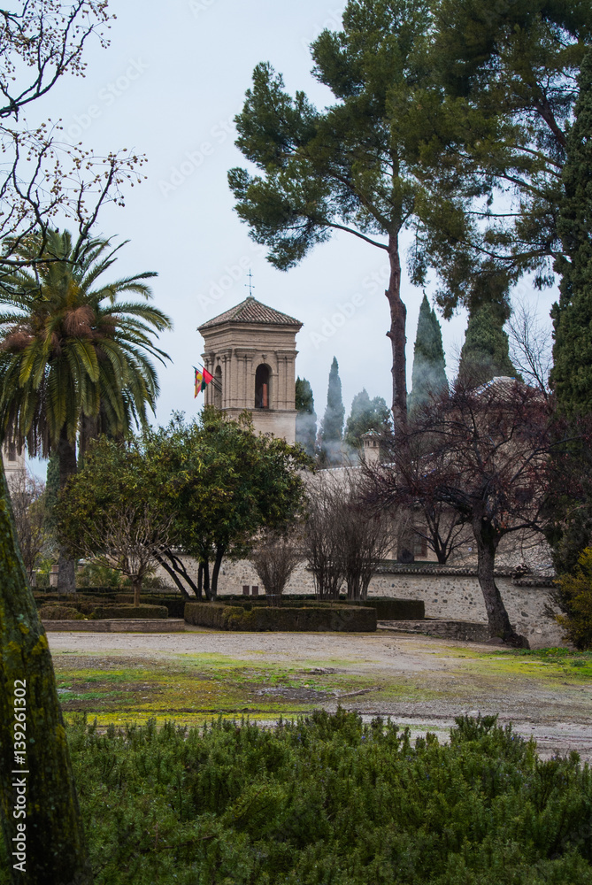 GRANADA, SPAIN - FEBRUARY 10, 2015: A view to a tower with flags on rainy foggy day at the yard of Alhambra, Granada, Andalusia, Spain. GRANADA, SPAIN - FEBRUARY 10, 2015: A view to a tower with flags on rainy foggy day at the yard of Alhambra, Granada, Andalusia, Spain.