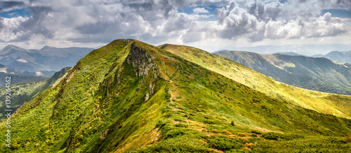Panoramic landscape of summer mountains. View of cliff tops and green hills.