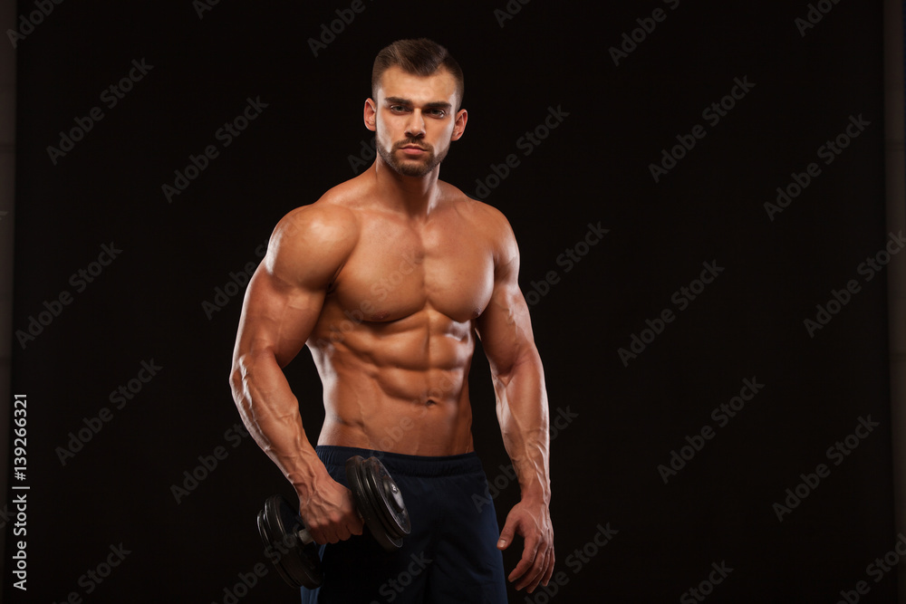 Handsome power athletic man with dumbbell is confidently looking forward. Strong bodybuilder with six pack, perfect abs, shoulders, biceps, triceps and chest Isolated on black background with