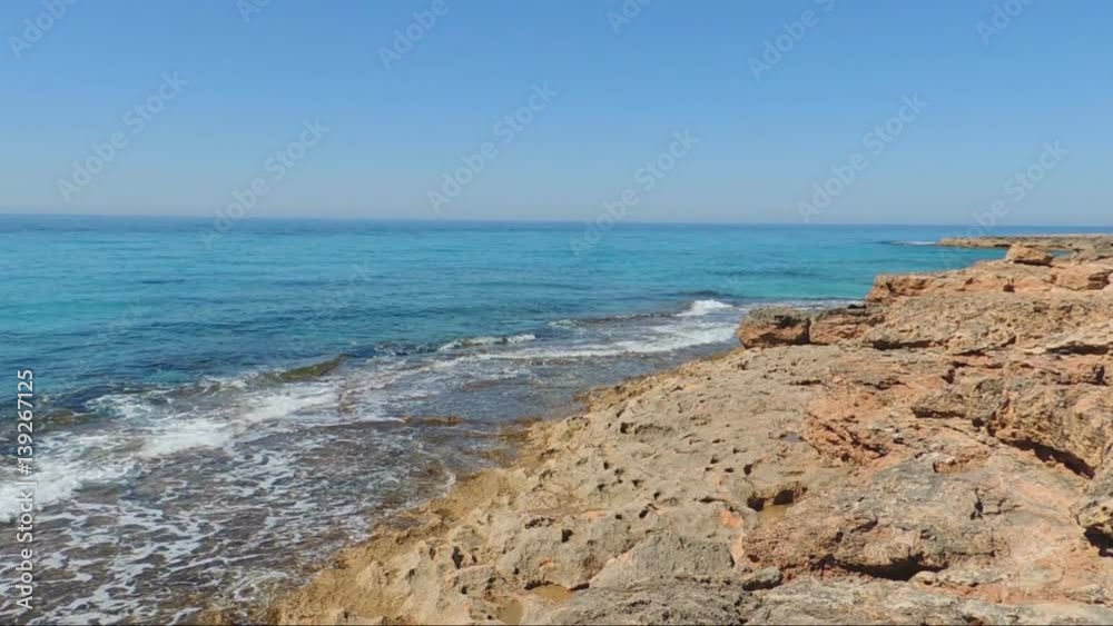 Cap De Ses Salines the most southern cape of Mallorca Island. Serene turquoise sea. Waves break into red stones. Cap De Ses Salines the most southern cape of Mallorca Island. Serene turquoise sea. Waves break into red stones.
