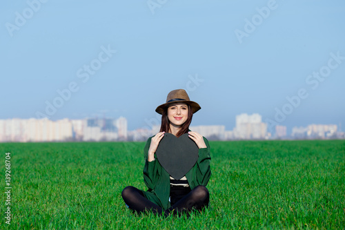 beautiful young woman sitting on the grass with heart shaped toy on the wonderful green field