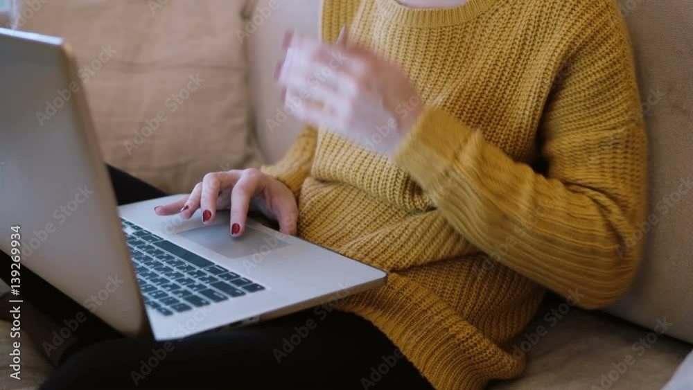 Woman s hands working on laptop sitting on the sofa at home.