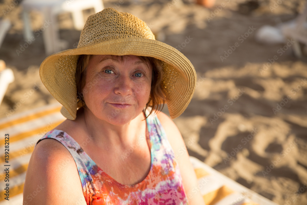 Smiling Senior woman wearing hat at beach on sunbed