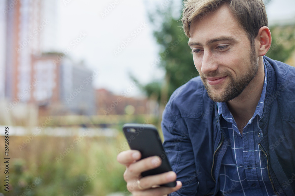 Man relaxing in park, looking at multimedia smartphone Man relaxing in park, looking at multimedia smartphone