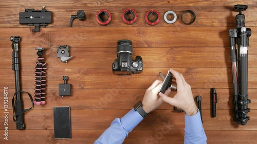 Man photographer LED light illuminates camera and shoots on phone. Wooden table top view. Equipment for shooting on the table