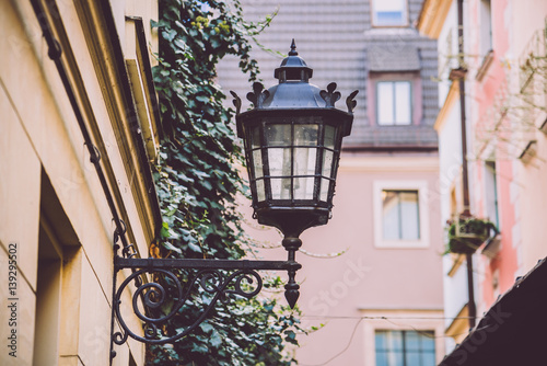 Close up view of the street lamp on the ancient wall in Wroclaw, Poland. Vintage iron lantern on green ivy and windows background.