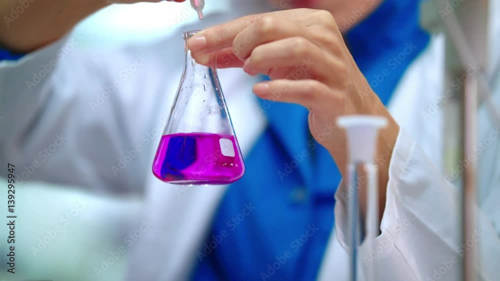 Medical lab worker dripping reagent in pink liquid. Medical researcher working with chemical liquid in lab flask. Medical lab experiment in lab beaker. Close up of laboratory testing in glass flask