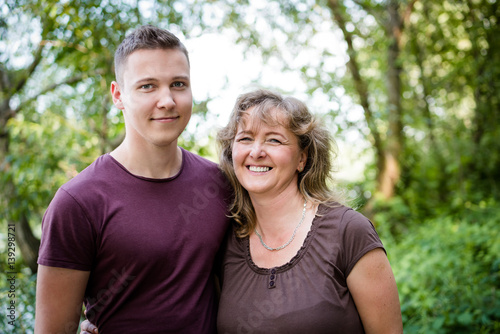 Smiling mother posing with adult son, outdoors.