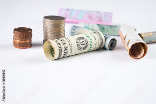 One hundred  US dollar and other currency rolled bills banknotes, with stacked coins isolated on white background. Exange rates concept photo