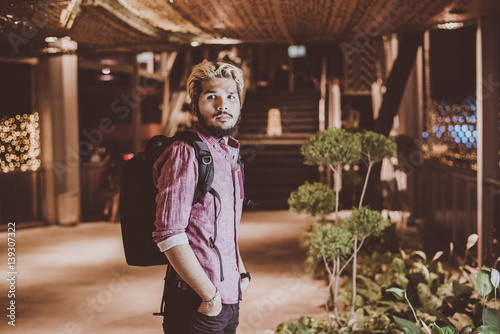 Handsome bearded man with backpack standing on the street while traveling at night.