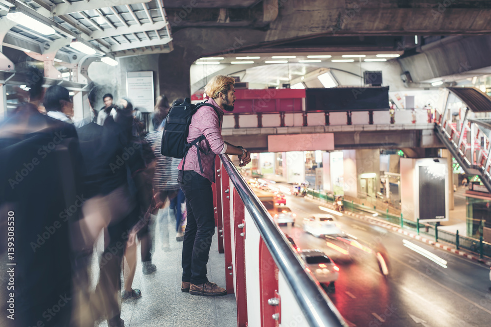 Fototapeta premium Hipster bearded man standing in the train station with people motion background while traveling at night.