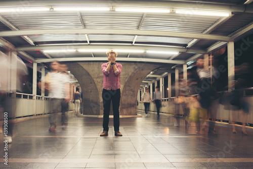 Hipster bearded man standing on the floor with people motion background while traveling at night.