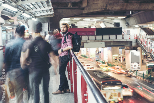 Hipster bearded man standing in the train station with people motion background while traveling at night.