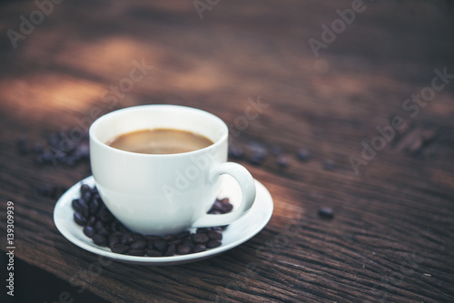 Close up a cup of coffee with coffee beans on wooden table.