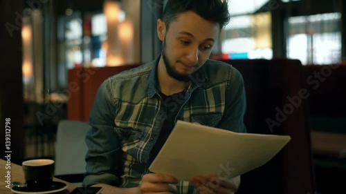Young boy reading notes aloud in the cafe and drinking coffee during break

