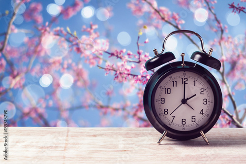 Spring time change concept with alarm clock over nature tree blossom background