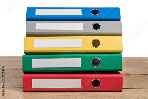Several multi-colored office folders lying in a stack on a wooden table isolated on white background