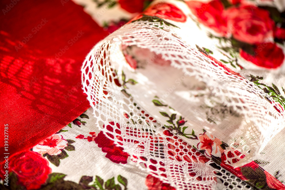 A macro shot of natural linen tablecloth with rose print and snow white crochet linen lace trim and red linen napkins. Shot is taken in the middle of autumn, during the sunset