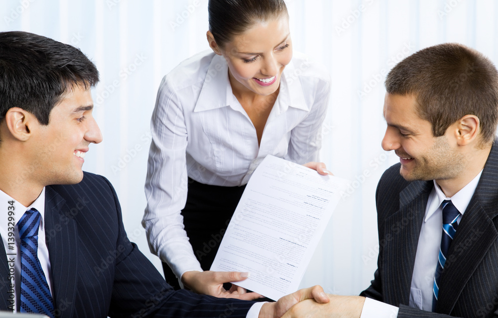 Businesspeople handshaking with document at office Businesspeople handshaking with document at office