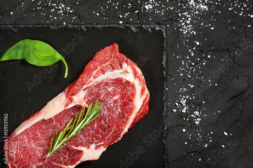 raw beef steak with rosemary and peppers on dark stone