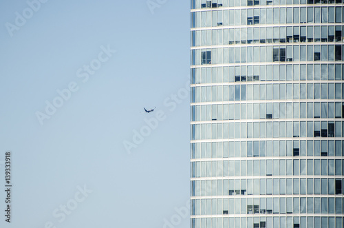 Abstract view of modern facade of skyscraper with closed and opened windows on clear blue sky background. A plane flies right in to the building, looks like it's going to crash in high-rise building